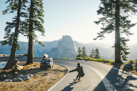 Rückansicht eines Mannes beim Skateboardfahren auf der Straße zwischen Bergen und klarem Himmel, lizenzfreies Stockfoto