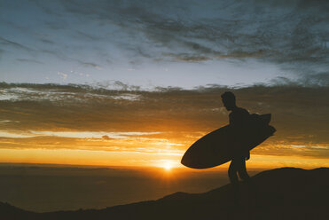 Man with surfboard on rocky shore by sea during sunset - CAVF28612