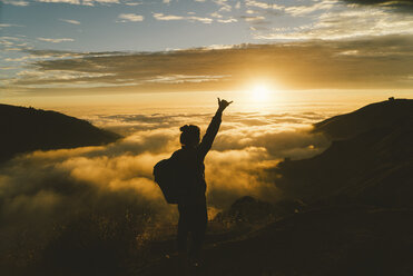 Silhouette einer Wanderin, die auf einem Berg bei Sonnenuntergang steht und gestikuliert - CAVF28630