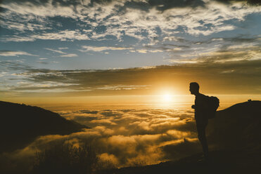 Silhouette männlicher Wanderer bei Sonnenuntergang auf einem Berg stehend - CAVF28631