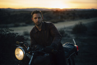 Porträt eines Mannes, der bei Sonnenuntergang auf einem Feld Motorrad fährt - CAVF28653