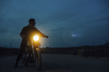 Low angle view of man riding illuminated motorcycle on street at dusk - CAVF28654