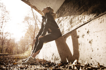 Tired woman resting on retaining wall in tunnel - CAVF28670