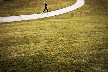 Sportler joggt auf einem Weg inmitten eines grasbewachsenen Feldes - CAVF28677