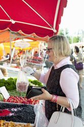 Lächelnde ältere Frau kauft Erdbeeren auf dem Straßenmarkt - FOLF01032
