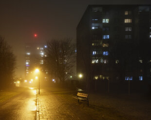 Beleuchtete Wohngebäude entlang einer leeren Straße im Nebel - FOLF01041