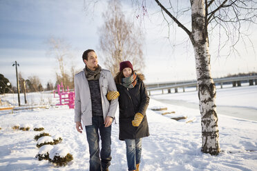 Junges Paar geht im Schnee am Fluss spazieren - FOLF01195