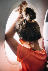 Rear view of girl looking through airplane window - CAVF28697