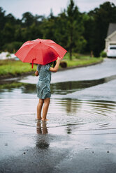 Rückansicht eines Mädchens, das einen Regenschirm hält und auf der Straße steht - CAVF28700