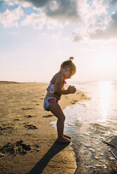 Happy girl playing with sand at beach against sky - CAVF28702