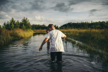 Playful siblings walking in canal against cloudy sky - CAVF28704