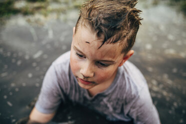 High angle view of messy boy sitting in puddle - CAVF28705