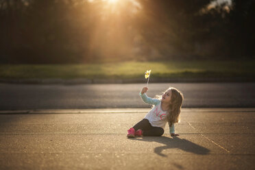 Fröhliches Mädchen spielt mit Windrädern auf einem Fußweg bei Sonnenuntergang - CAVF28745