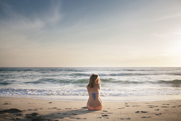 Rückansicht einer am Strand sitzenden Frau gegen den Himmel bei Sonnenuntergang - CAVF28768
