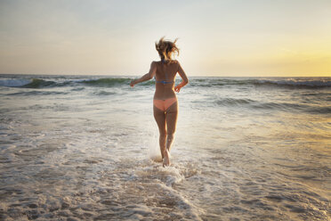 Rückansicht einer Frau, die bei Sonnenuntergang am Strand läuft - CAVF28769