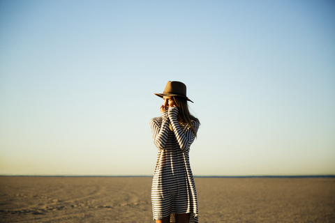 Nachdenkliche Frau am Strand stehend vor blauem Himmel, lizenzfreies Stockfoto