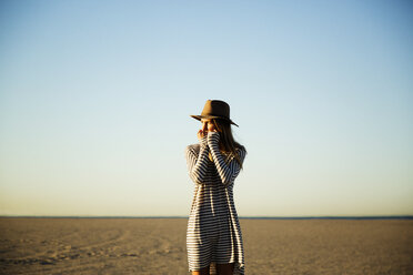 Nachdenkliche Frau am Strand stehend vor blauem Himmel - CAVF28789