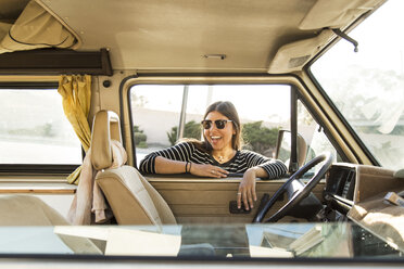 Cheerful woman leaning on mini van window during vacation - CAVF28804