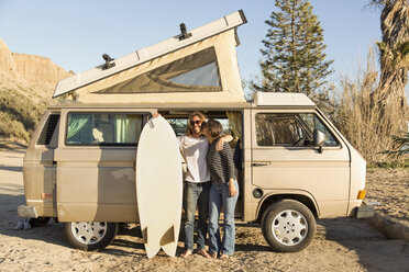 Loving woman kissing man holding surfboard in front of mini van on San Onofre State Beach - CAVF28810