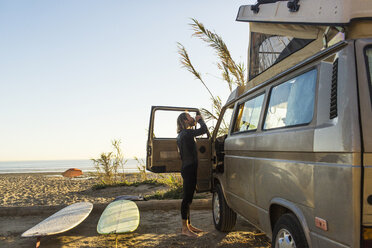 Seitenansicht eines männlichen Surfers, der vor einem Minivan am San Onofre State Beach etwas trinkt - CAVF28814