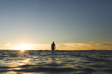 Distant view of female surfer on sea against sky during sunset - CAVF28816