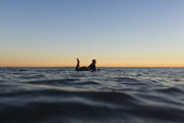 Seitenansicht einer Frau, die bei Sonnenuntergang auf einem Surfbrett im Meer liegt - CAVF28819