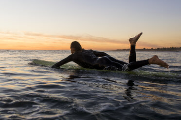 Seitenansicht eines Mannes, der bei Sonnenuntergang auf einem Surfbrett im Meer liegt - CAVF28822