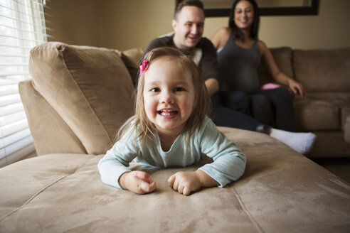 Porträt eines süßen Mädchens, während die Eltern zu Hause auf dem Sofa sitzen - CAVF28851