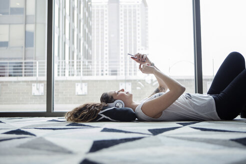 Young female using smart phone while lying on carpet by window at home - CAVF28887