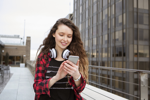 Junge Frau benutzt ihr Smartphone beim Spaziergang in einem Terrassencafé, lizenzfreies Stockfoto