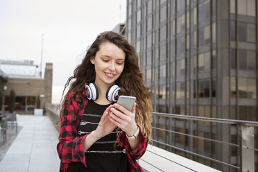 Junge Frau benutzt ihr Smartphone beim Spaziergang in einem Terrassencafé - CAVF28894