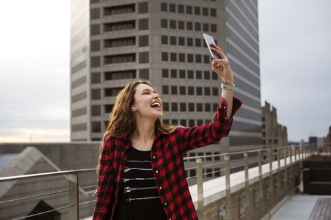 Cheerful young woman taking selfie while standing on terrace against building stock photo