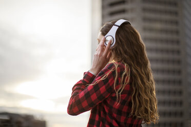 Side view of woman wearing headphones while standing against building - CAVF28903