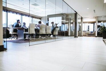 Businesswoman giving presentation in conference room seen through glass window - CAVF28925