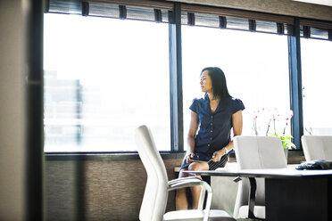 Nachdenkliche Geschäftsfrau, die durch das Fenster schaut, während sie im Büro sitzt - CAVF28942