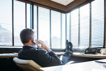 Geschäftsmann spricht mit seinem Smartphone, während er sich im Büro entspannt - CAVF28951
