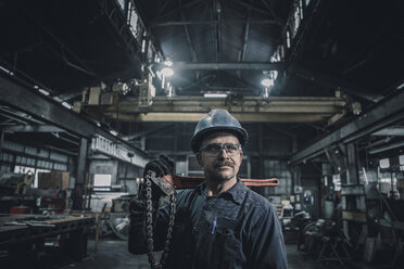 Male worker carrying work tool looking away while standing in factory - CAVF28963