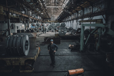 Hoher Blickwinkel eines männlichen Arbeiters, der in einer Fabrik vor Stahlblechen steht - CAVF28980