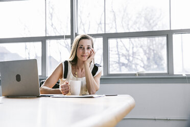 Portrait of businesswoman holding drink while sitting at table in board room - CAVF29059