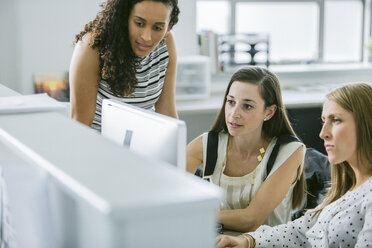 Female colleagues looking at desktop computer while working at desk in office - CAVF29063