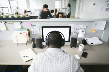 Rückansicht eines Geschäftsmannes, der an einem Desktop-Computer arbeitet, mit Kollegen im Hintergrund - CAVF29078