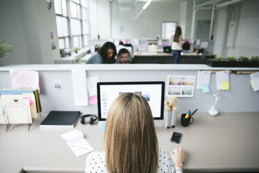Rückansicht einer Geschäftsfrau, die einen Desktop-Computer mit Kollegen im Hintergrund benutzt - CAVF29079