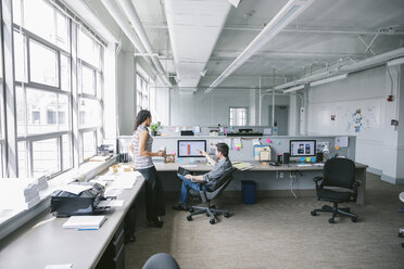 Businesswoman looking at businessman using desktop computer in office - CAVF29087