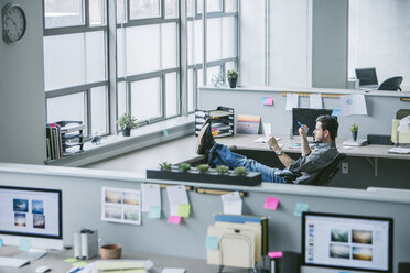 High angle view of businessman reading document while relaxing on chair in office - CAVF29094