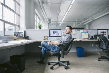 Seitenansicht eines Geschäftsmannes mit Tablet-Computer, der wegschaut, während er sich auf einem Stuhl entspannt - CAVF29098