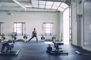 Young woman stretching legs against wall in health club - CAVF29109