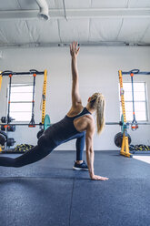 Rear view of woman stretching arms while exercising against wall in gym - CAVF29113