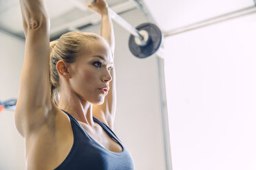 Nahaufnahme einer jungen Frau, die eine Langhantel hebt, während sie in einem hell erleuchteten Fitnessstudio trainiert - CAVF29119