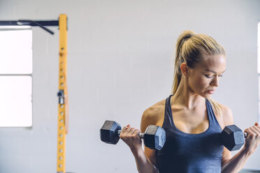 Junge Frau hebt Hanteln, während sie in einem Fitnessstudio an der Wand trainiert - CAVF29121