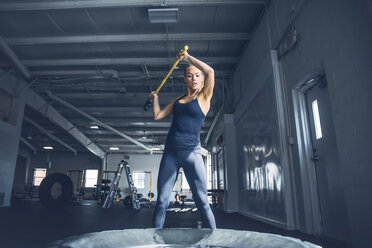 Frau schlägt beim Training im Fitnessstudio mit Vorschlaghammer auf Reifen ein - CAVF29124